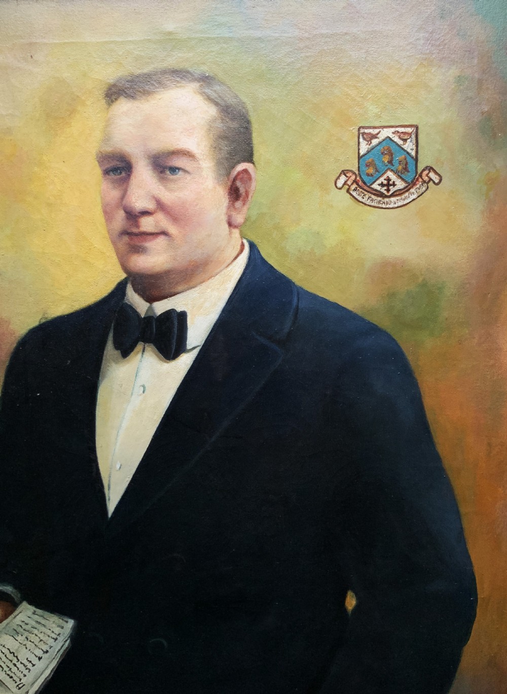 A framed oil portrait painting depicting a gentleman in a dark suit holding a paper document beside a small coat of arms. View IV