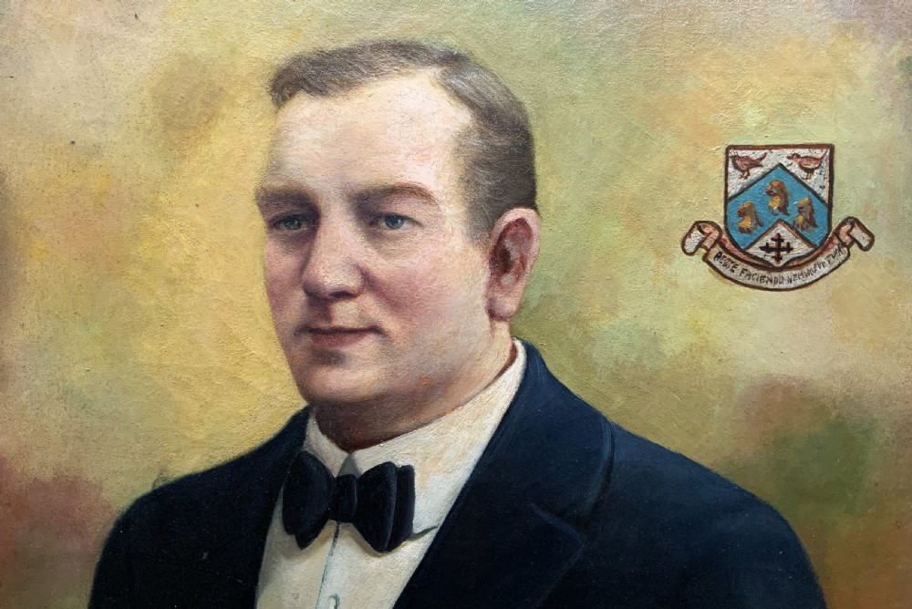A framed oil portrait painting depicting a gentleman in a dark suit holding a paper document beside a small coat of arms. View V