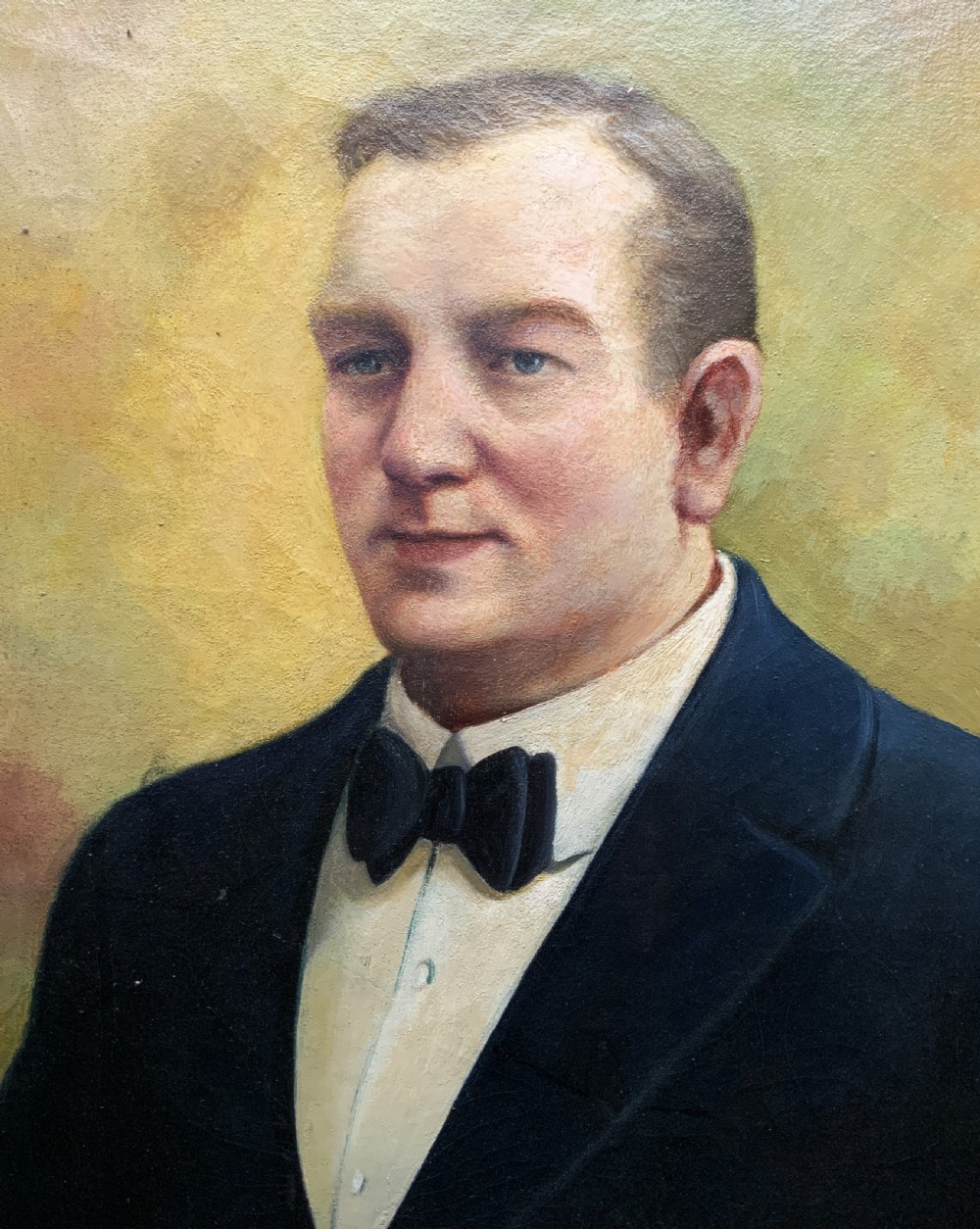 A framed oil portrait painting depicting a gentleman in a dark suit holding a paper document beside a small coat of arms. View VI