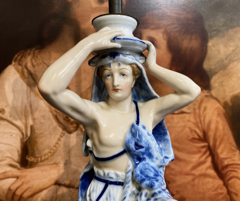 An Art Deco blue and white porcelain table lamp featuring a sculpted male figure on a decorative pedestal with a twin brass light socket stem. View VIII