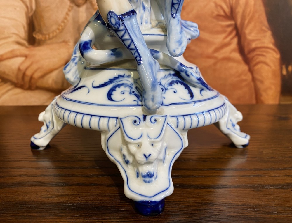 An Art Deco blue and white porcelain table lamp featuring a sculpted male figure on a decorative pedestal with a twin brass light socket stem. View X