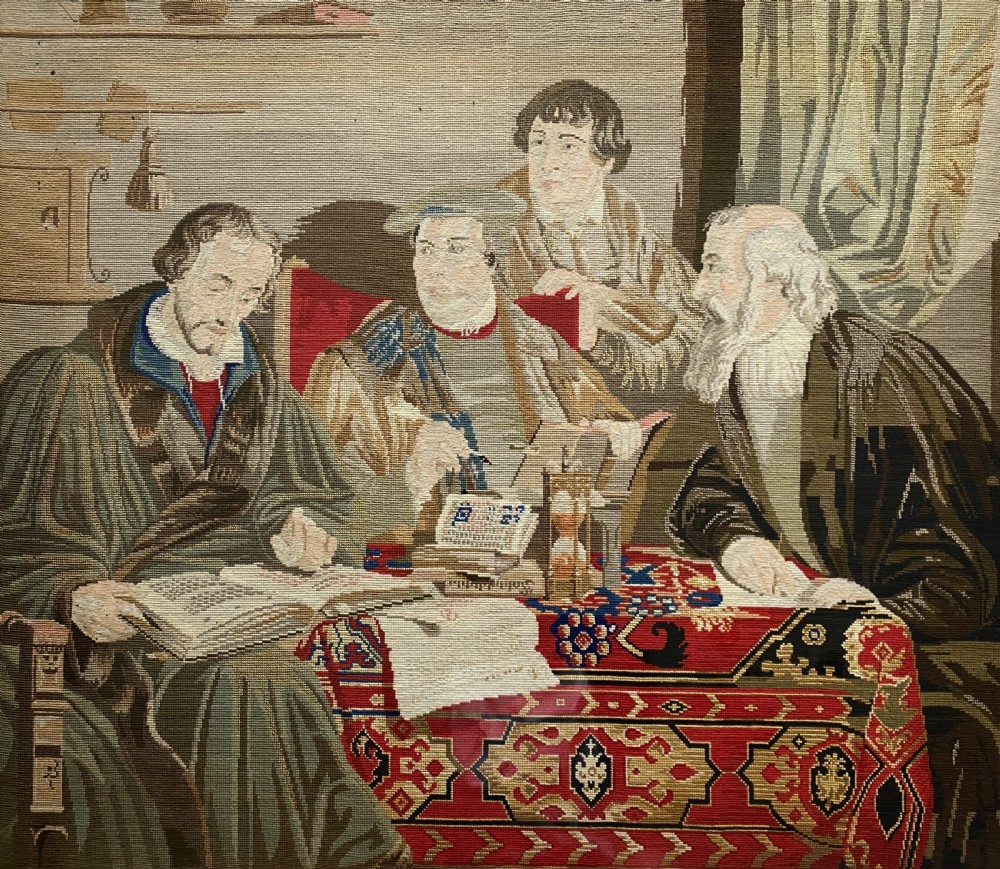 A framed mid-nineteenth-century Berlin woolwork tapestry depicting four historical figures seated around a carpet-covered table, housed within a gilt decorative frame. View II