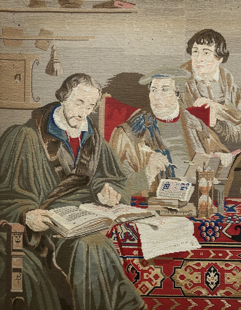 A framed mid-nineteenth-century Berlin woolwork tapestry depicting four historical figures seated around a carpet-covered table, housed within a gilt decorative frame. View VI