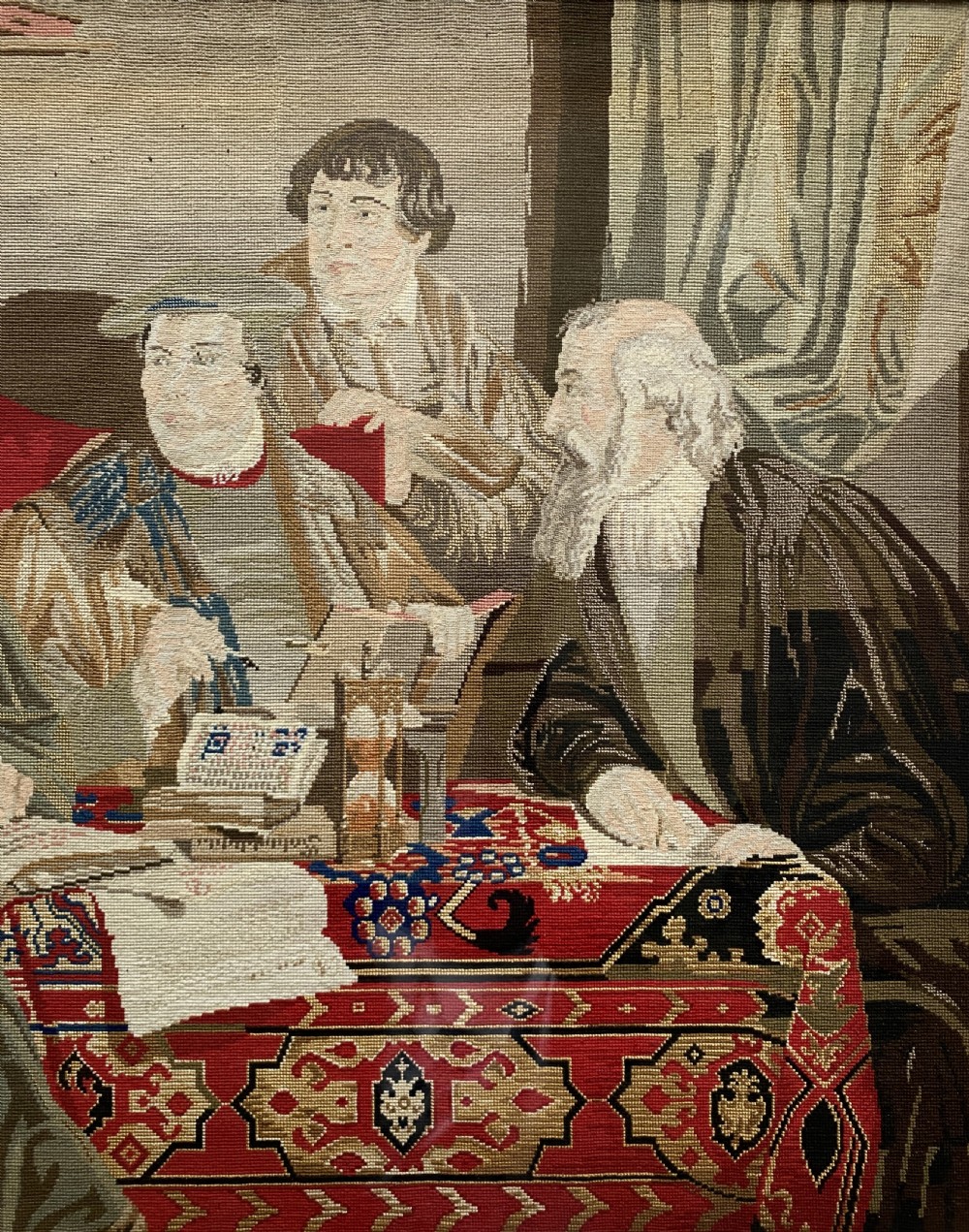 A framed mid-nineteenth-century Berlin woolwork tapestry depicting four historical figures seated around a carpet-covered table, housed within a gilt decorative frame. View VII