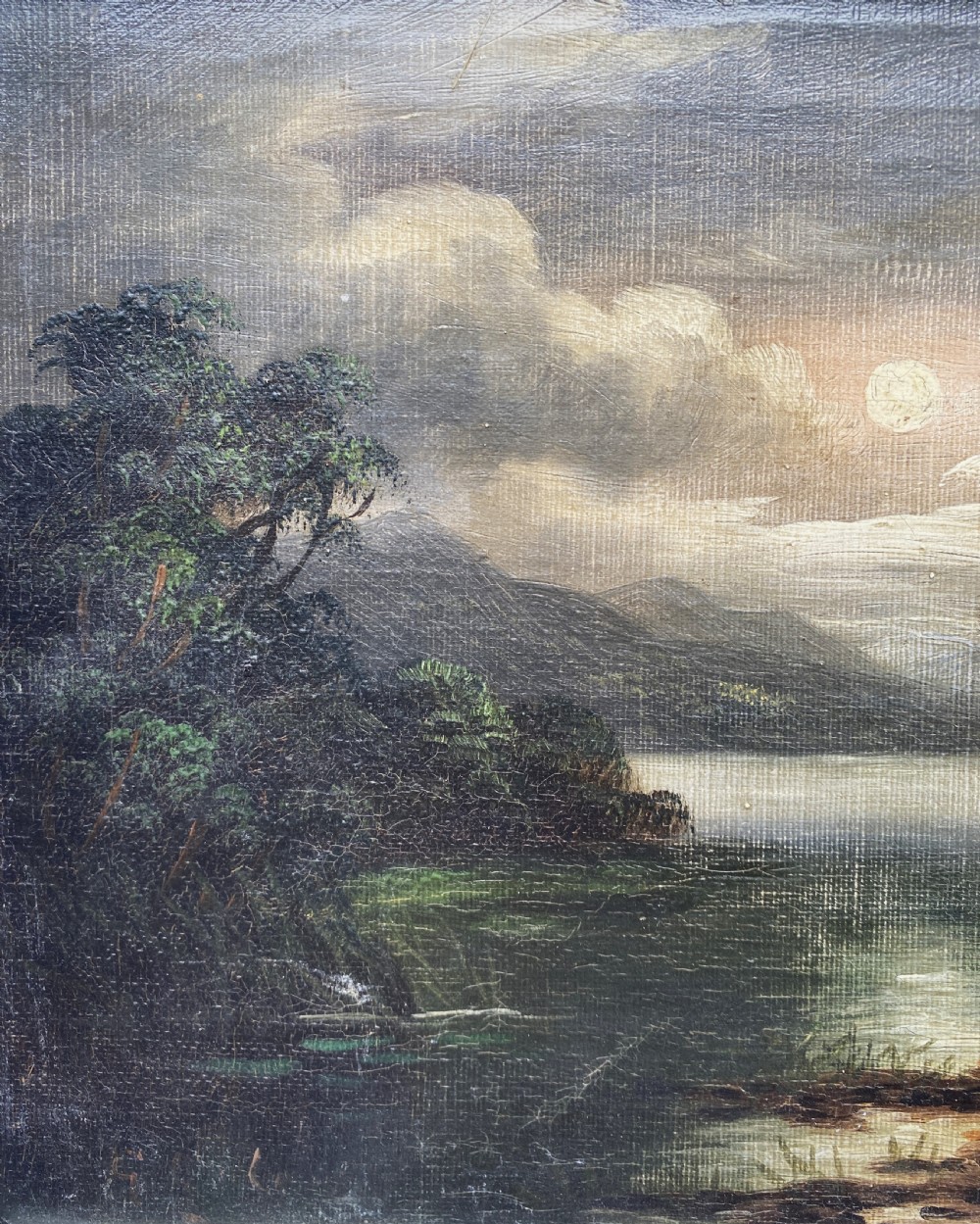 An oil painting depicting a moonlit highland loch scene with a small cottage near the water, framed in a thick white painted wooden frame. View VI