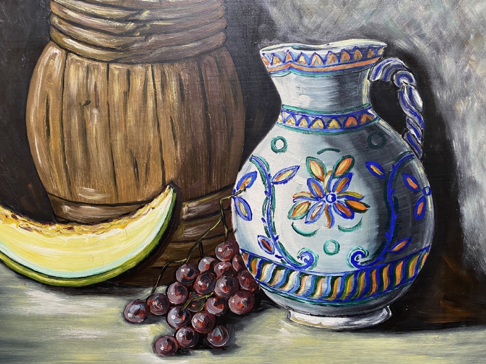 A framed mid-century oil painting depicting a still life composition with a blue patterned ceramic jug, a wooden barrel, a melon slice, and purple grapes. View III