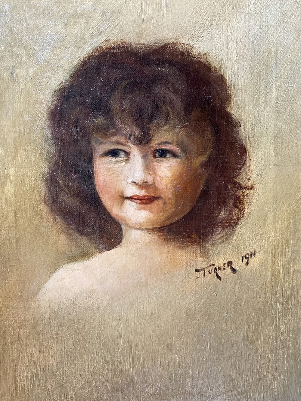 An early twentieth-century oil painting depicting a young girl with brown curly hair, framed within a wide moulded gold gilt frame. View III