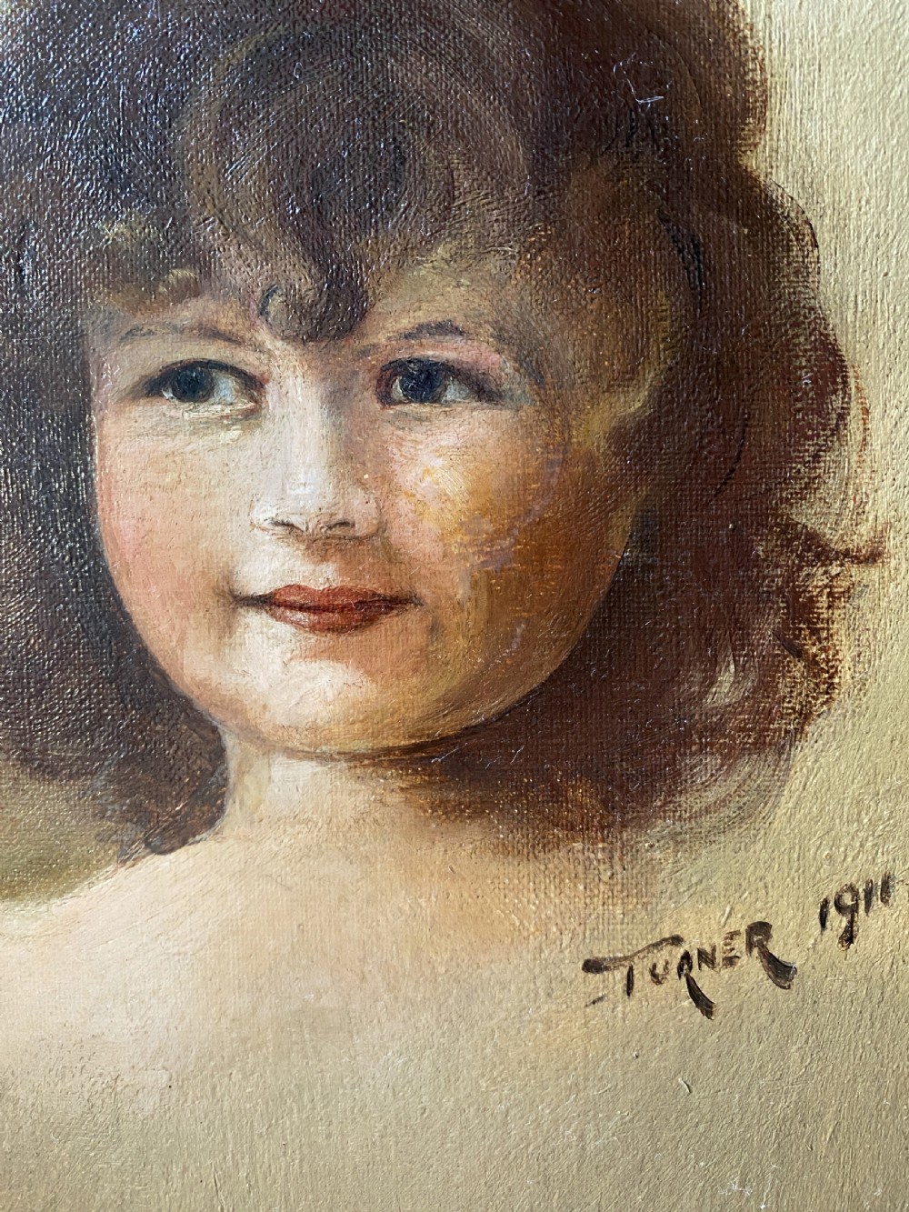An early twentieth-century oil painting depicting a young girl with brown curly hair, framed within a wide moulded gold gilt frame. View VII
