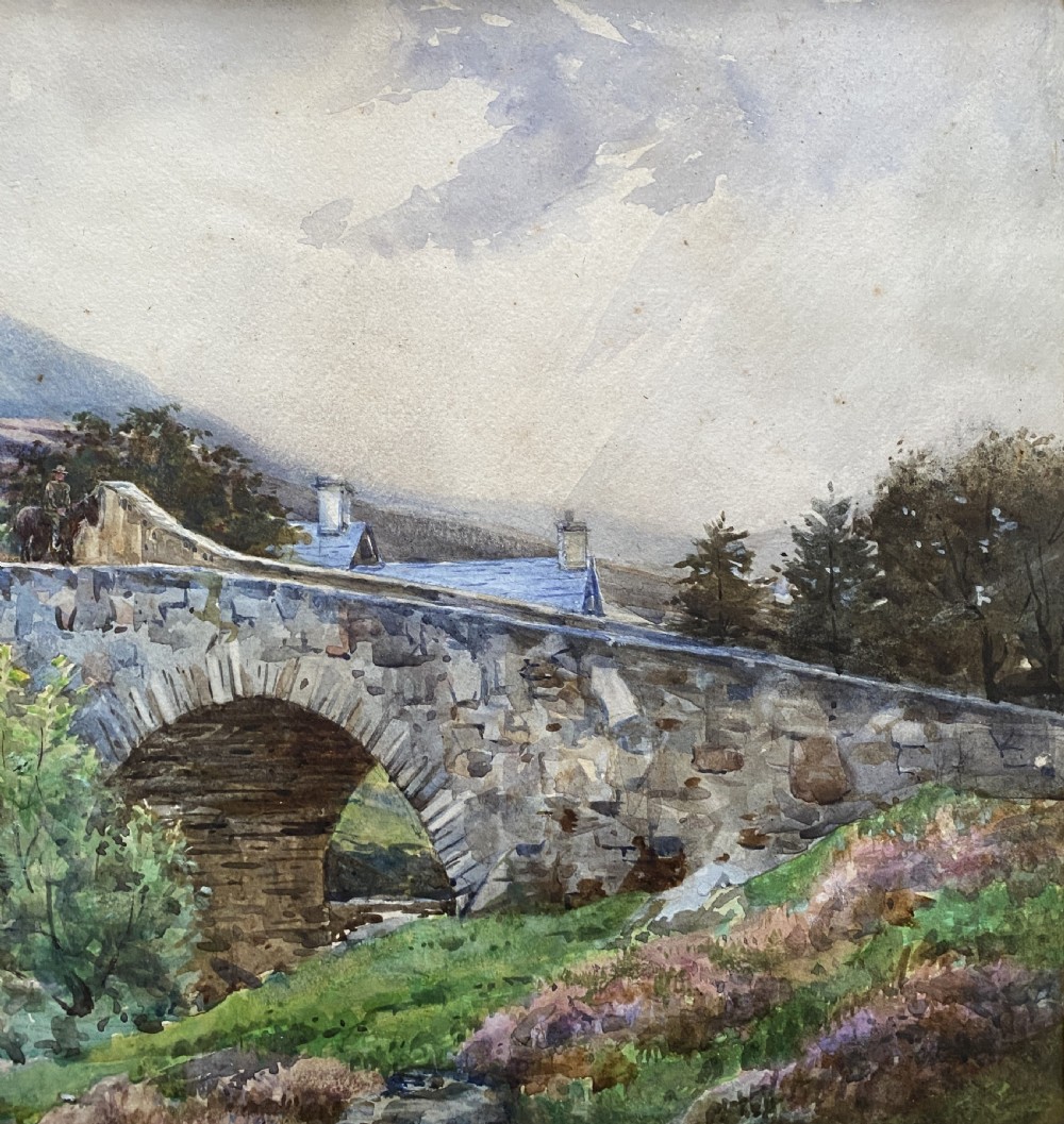 An early 20th-century watercolour painting depicting a stone arch bridge over a river surrounded by hills, set within a wide gold frame. View III