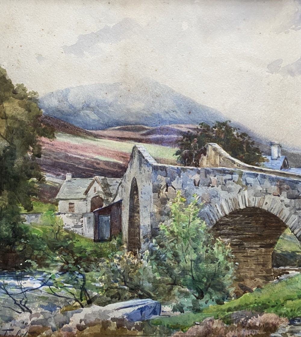 An early 20th-century watercolour painting depicting a stone arch bridge over a river surrounded by hills, set within a wide gold frame. View V