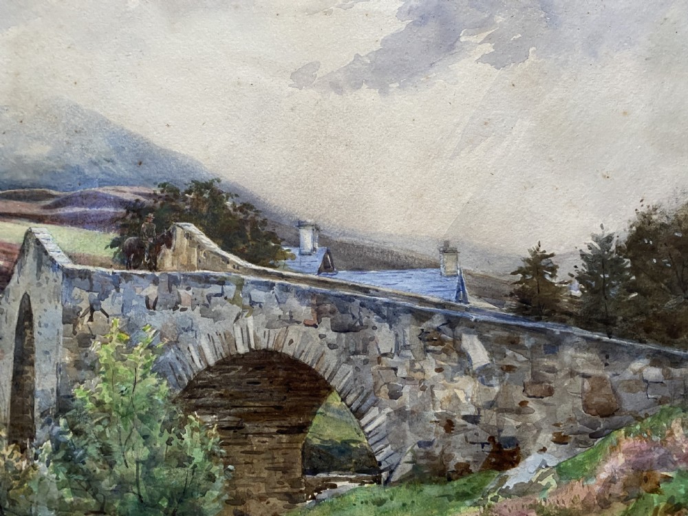 An early 20th-century watercolour painting depicting a stone arch bridge over a river surrounded by hills, set within a wide gold frame. View VII