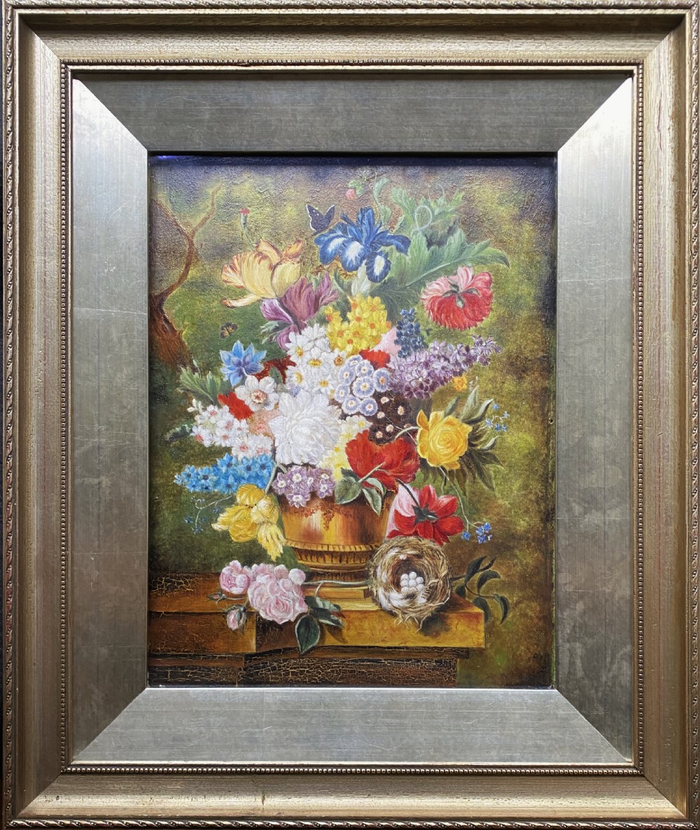 A framed oil painting featuring a floral bouquet in an urn set upon a ledge next to a bird nest.