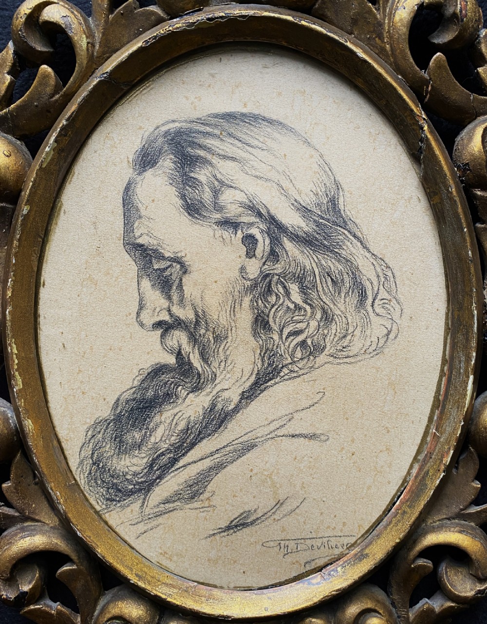 An oval charcoal profile drawing on paper depicting a bearded man with long hair, set inside a carved gold leaf Florentine frame.