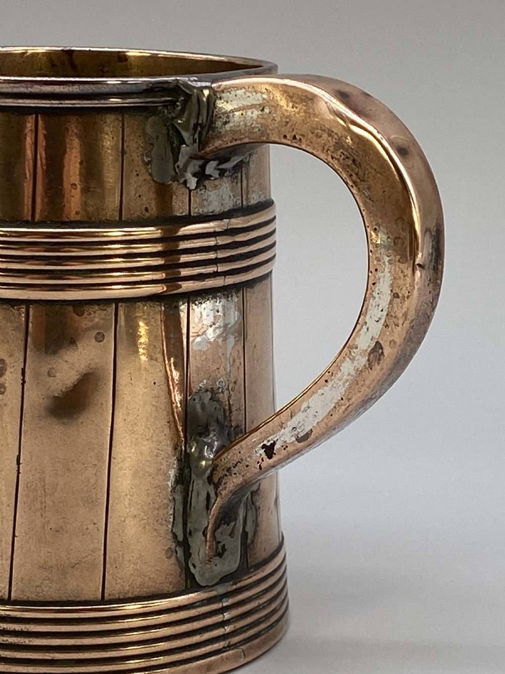 A tapered late Georgian copper tankard featuring horizontal reeded bands, vertical staved lines, and a curved nickel-plated handle. View X
