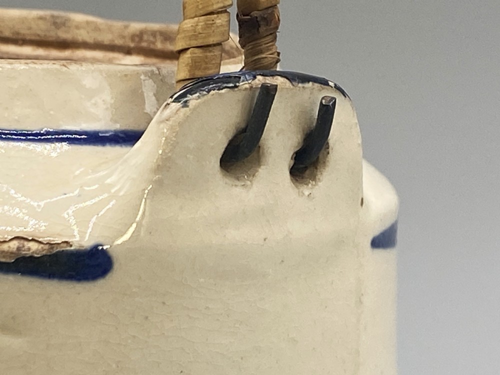 A cylindrical cream-coloured ceramic teapot decorated with hand-painted blue cobalt landscapes and featuring an overhead woven cane handle. View XVII