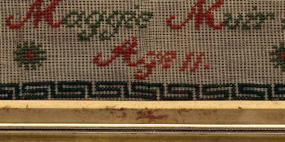 A vertical Victorian framed sampler featuring rows of embroidered alphabets in red and green wool thread on linen fabric, housed within a gilded wooden frame. View IX