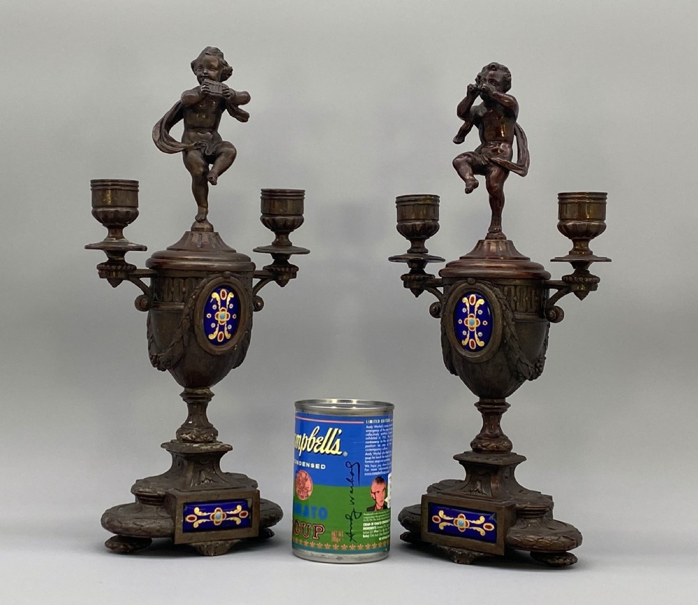 A pair of late 19th-century bronzed spelter twin-light candelabra featuring putti surmounts and urn-shaped bodies set with blue enamel plaques. View II