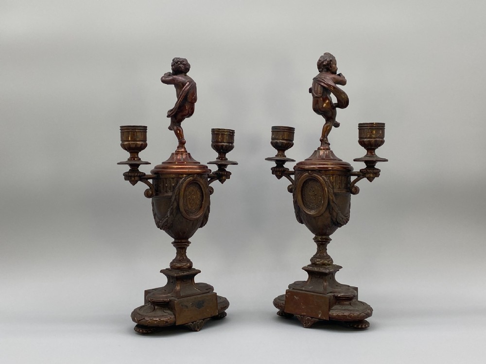 A pair of late 19th-century bronzed spelter twin-light candelabra featuring putti surmounts and urn-shaped bodies set with blue enamel plaques. View V