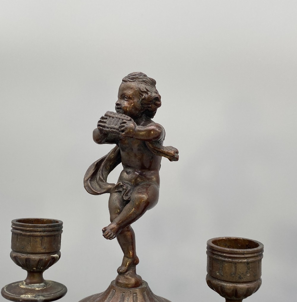 A pair of late 19th-century bronzed spelter twin-light candelabra featuring putti surmounts and urn-shaped bodies set with blue enamel plaques. View VI