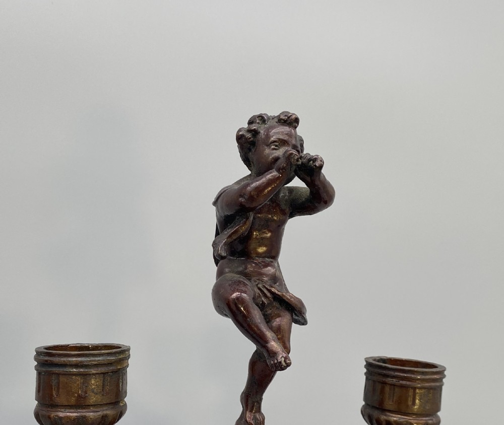 A pair of late 19th-century bronzed spelter twin-light candelabra featuring putti surmounts and urn-shaped bodies set with blue enamel plaques. View VII