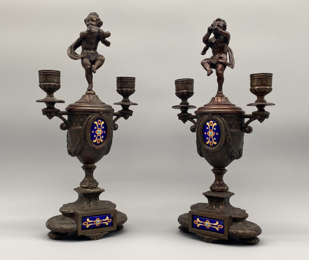 A pair of late 19th-century bronzed spelter twin-light candelabra featuring putti surmounts and urn-shaped bodies set with blue enamel plaques. View XI