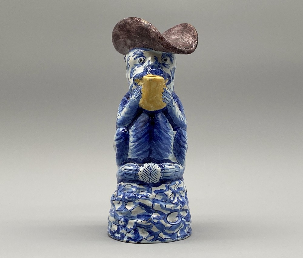 An eighteenth-century Dutch Delft tin-glazed earthenware jug shaped as a seated monkey wearing a hat and holding a vessel, decorated in blue, white, brown, and yellow glazes. View V
