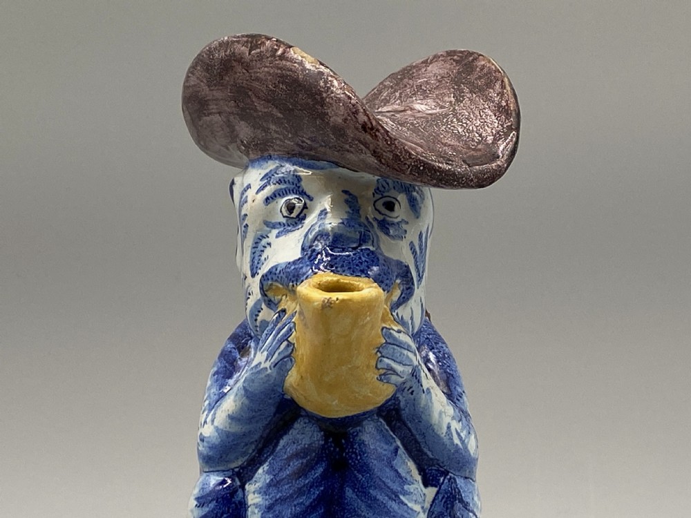 An eighteenth-century Dutch Delft tin-glazed earthenware jug shaped as a seated monkey wearing a hat and holding a vessel, decorated in blue, white, brown, and yellow glazes. View VI