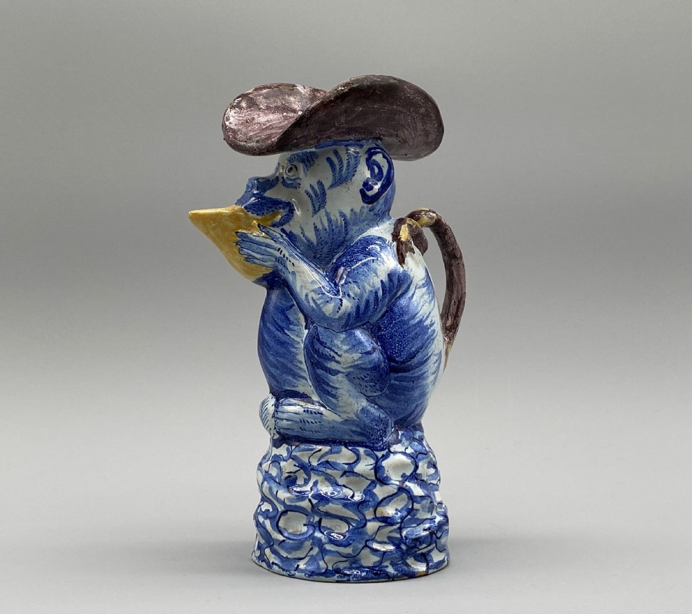 An eighteenth-century Dutch Delft tin-glazed earthenware jug shaped as a seated monkey wearing a hat and holding a vessel, decorated in blue, white, brown, and yellow glazes. View VII