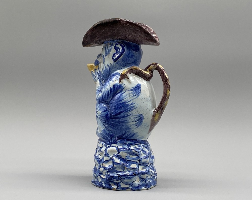 An eighteenth-century Dutch Delft tin-glazed earthenware jug shaped as a seated monkey wearing a hat and holding a vessel, decorated in blue, white, brown, and yellow glazes. View VIII