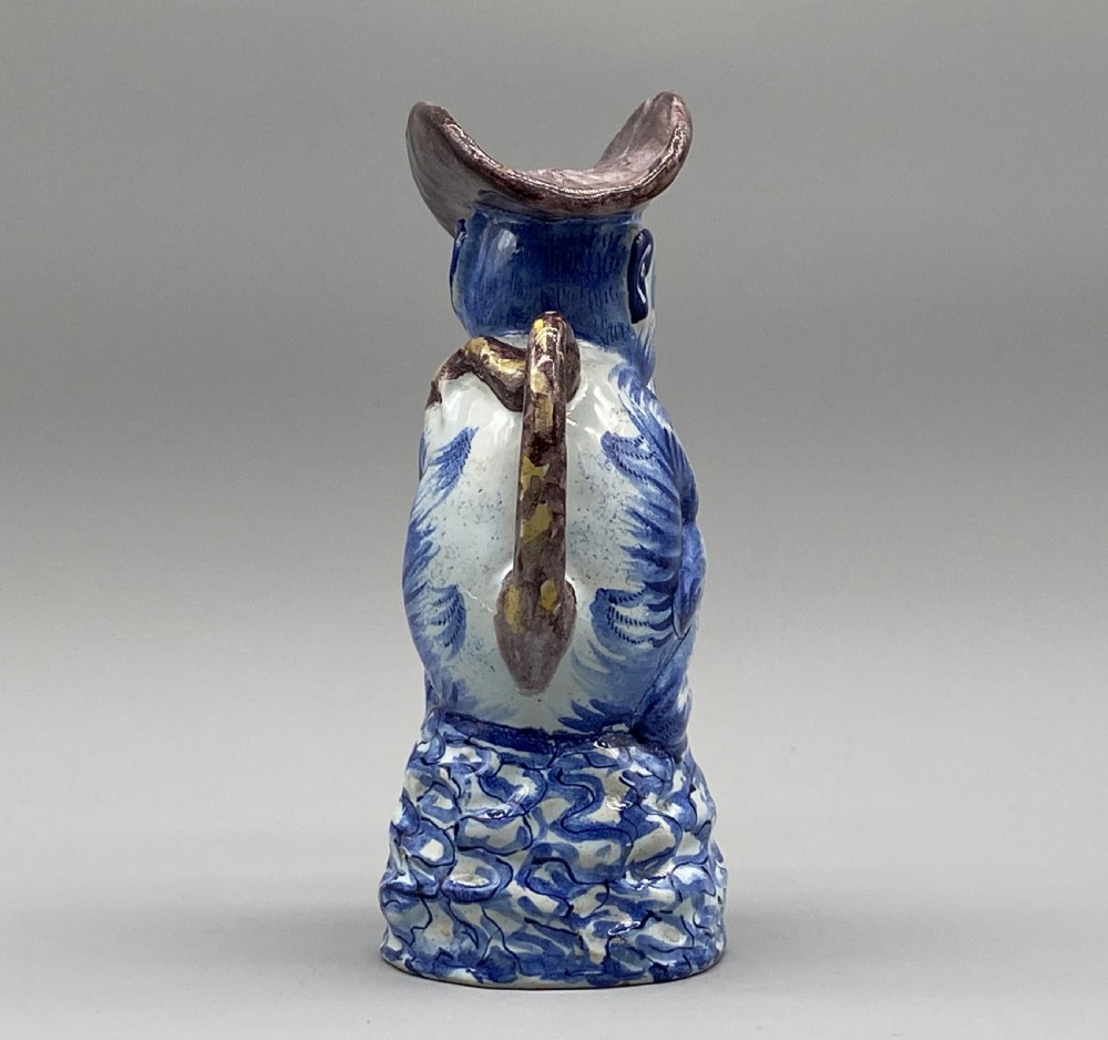 An eighteenth-century Dutch Delft tin-glazed earthenware jug shaped as a seated monkey wearing a hat and holding a vessel, decorated in blue, white, brown, and yellow glazes. View IX