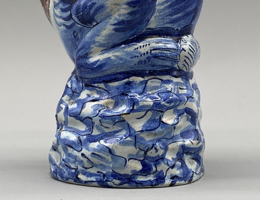 An eighteenth-century Dutch Delft tin-glazed earthenware jug shaped as a seated monkey wearing a hat and holding a vessel, decorated in blue, white, brown, and yellow glazes. View XII