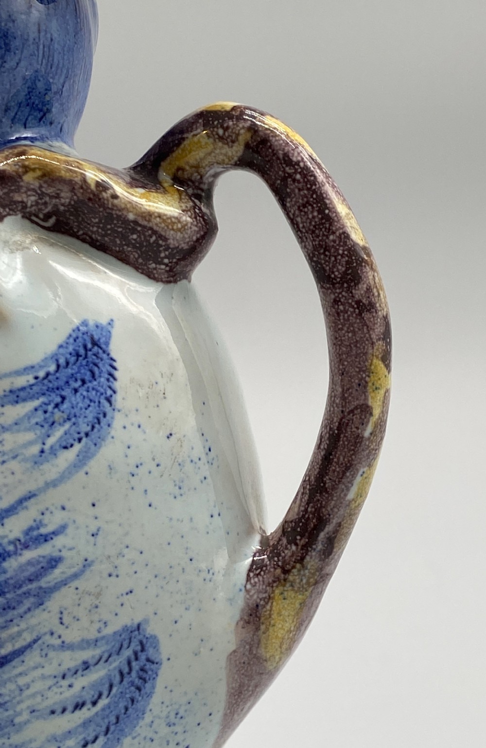 An eighteenth-century Dutch Delft tin-glazed earthenware jug shaped as a seated monkey wearing a hat and holding a vessel, decorated in blue, white, brown, and yellow glazes. View XVI
