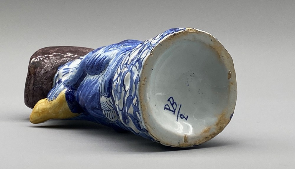 An eighteenth-century Dutch Delft tin-glazed earthenware jug shaped as a seated monkey wearing a hat and holding a vessel, decorated in blue, white, brown, and yellow glazes. View XVIII
