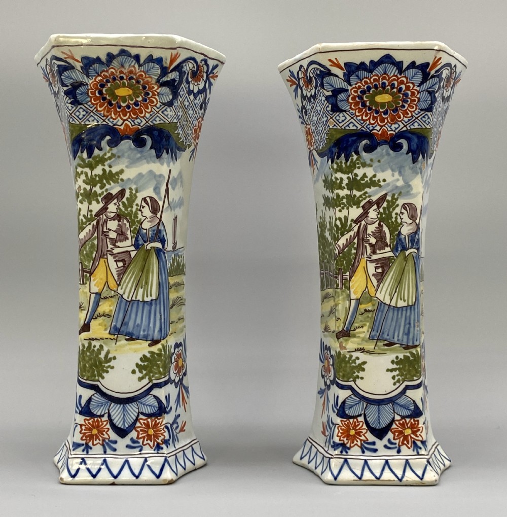 A pair of 18th-century octagonal flared Dutch Delft polychrome tin-glazed earthenware vases featuring hand-painted pastoral scenes of figures in landscape settings framed by floral motifs.
