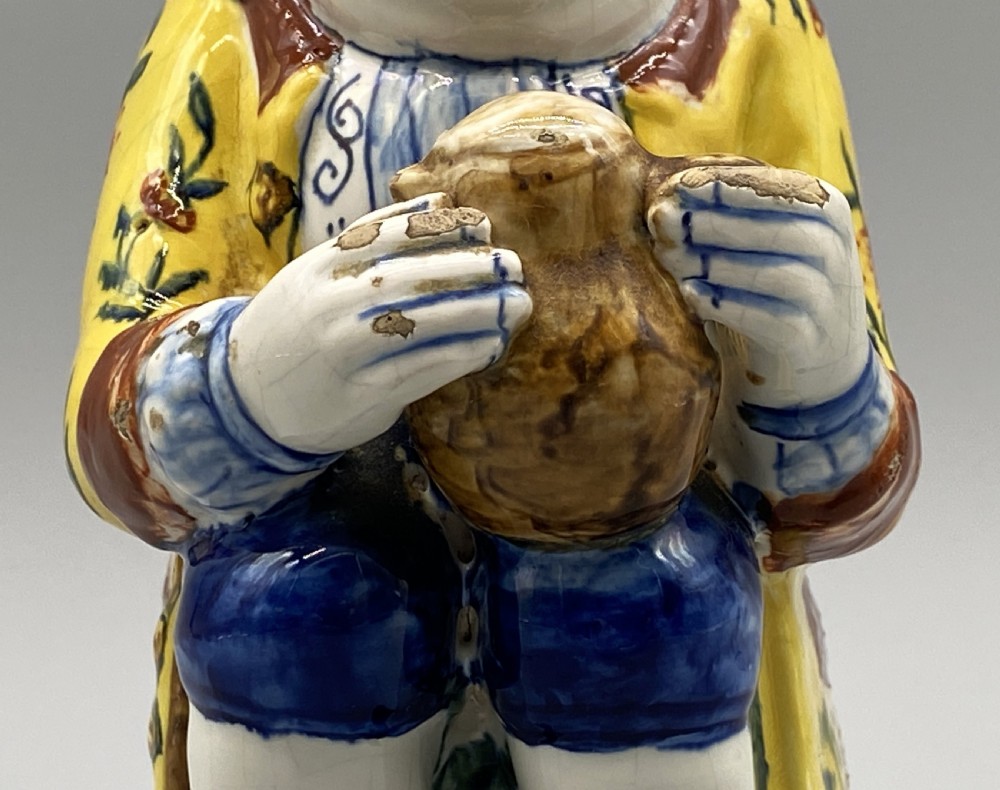 A polychrome tin-glazed earthenware Toby jug depicting a seated figure in a tricorn hat and yellow floral coat holding a small pitcher. View XII