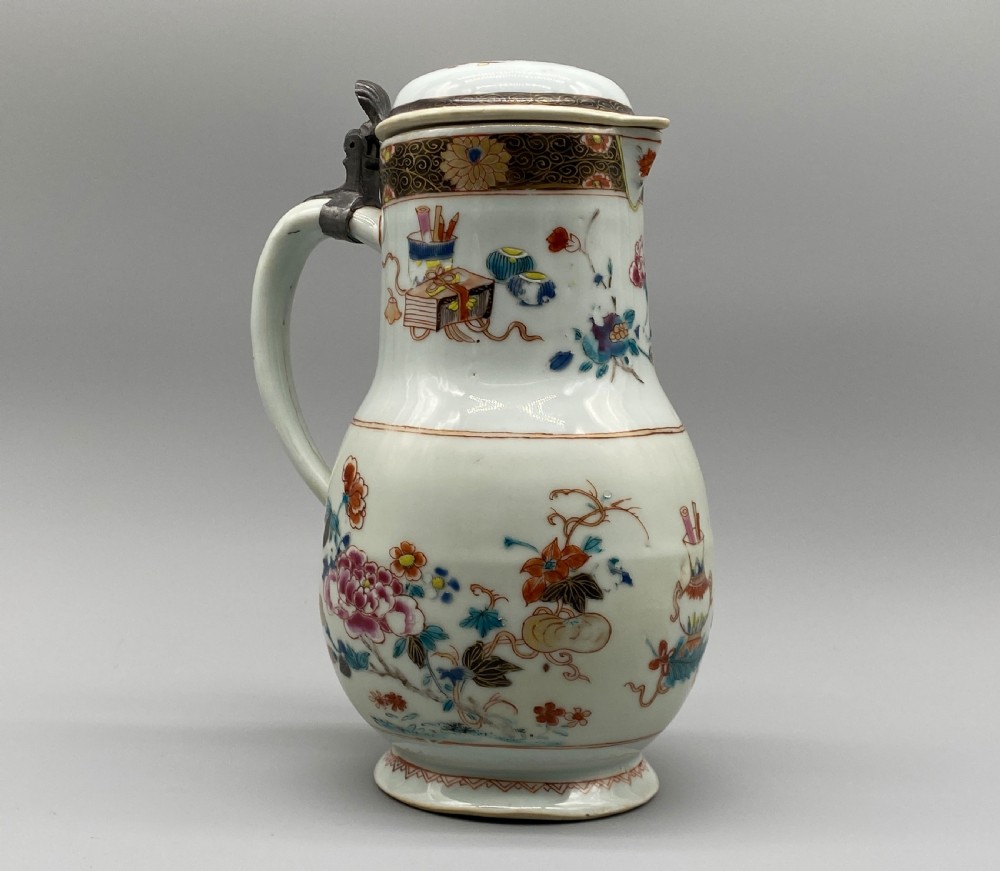 An 18th-century Chinese porcelain jug with hand-painted Famille Rose floral enamels, a metal-mounted lid, and a loop handle. View V