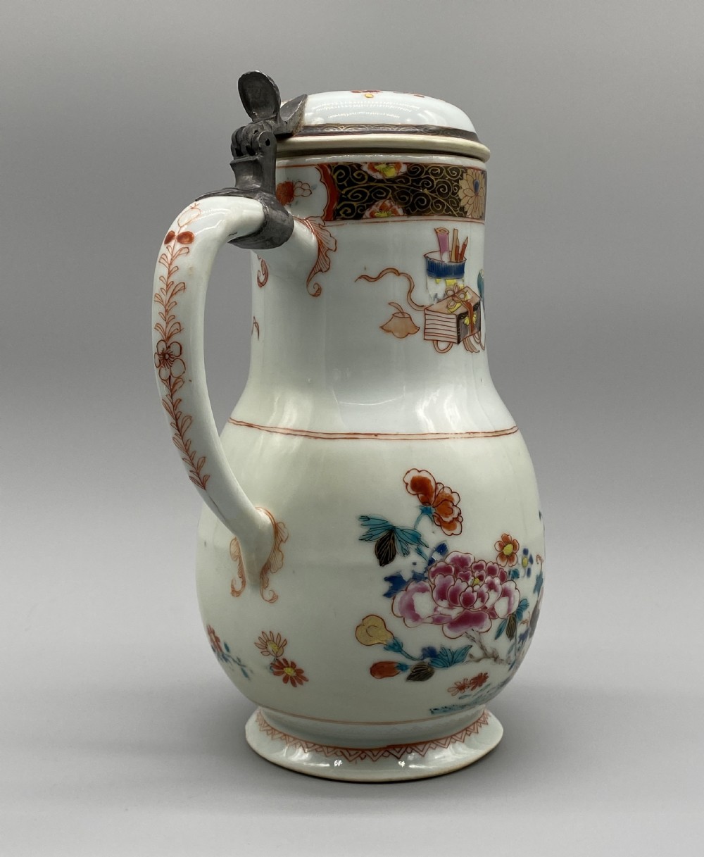 An 18th-century Chinese porcelain jug with hand-painted Famille Rose floral enamels, a metal-mounted lid, and a loop handle. View VI