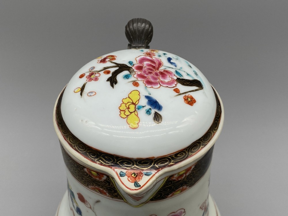 An 18th-century Chinese porcelain jug with hand-painted Famille Rose floral enamels, a metal-mounted lid, and a loop handle. View VIII