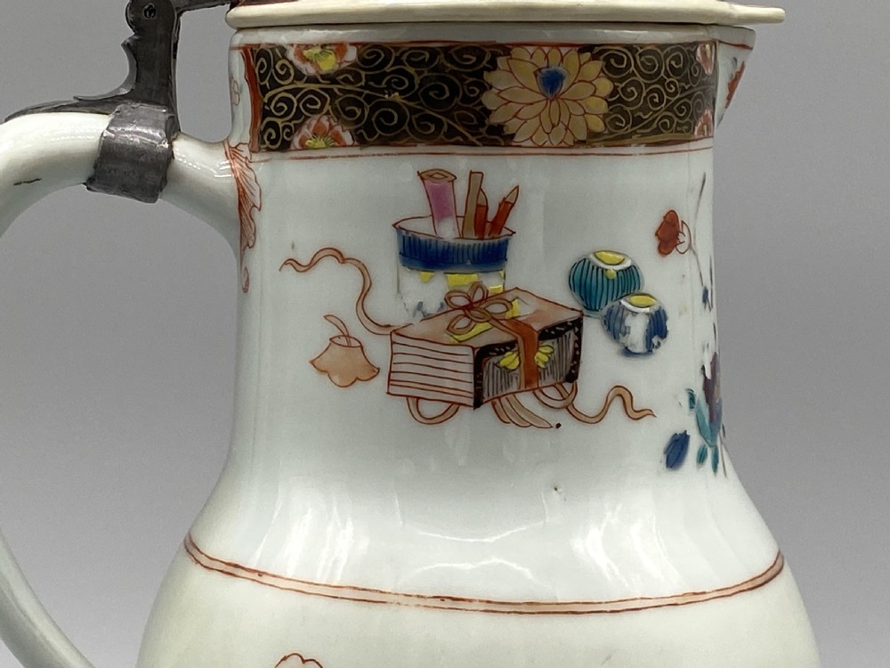An 18th-century Chinese porcelain jug with hand-painted Famille Rose floral enamels, a metal-mounted lid, and a loop handle. View XII