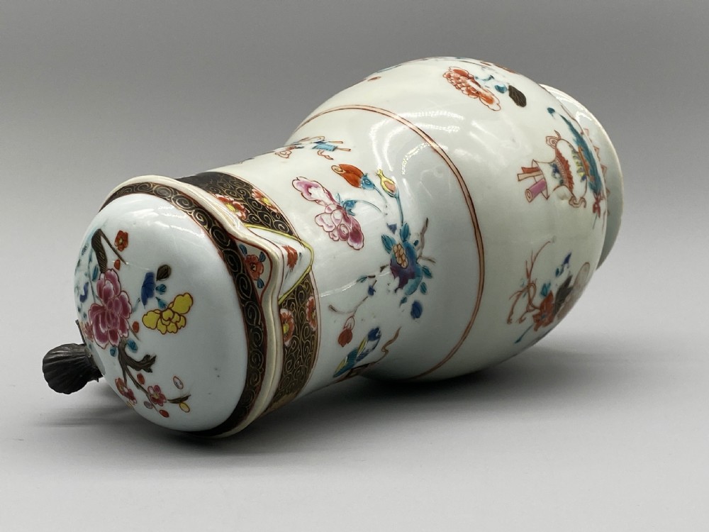 An 18th-century Chinese porcelain jug with hand-painted Famille Rose floral enamels, a metal-mounted lid, and a loop handle. View XIX