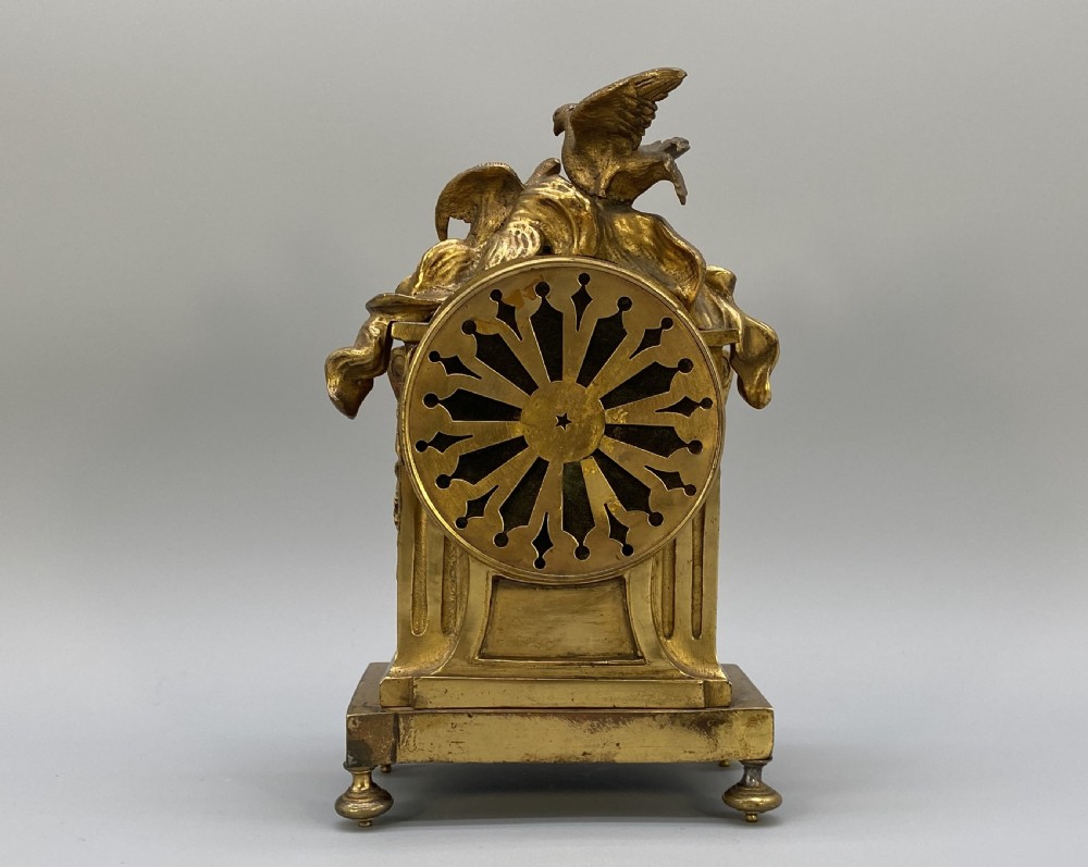 An antique French gilt bronze mantel clock surmounted by two sculpted doves, featuring an ornate pedestal base and a white enamel dial with Roman numerals. View VI
