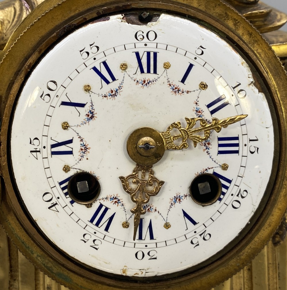 An antique French gilt bronze mantel clock surmounted by two sculpted doves, featuring an ornate pedestal base and a white enamel dial with Roman numerals. View XIV