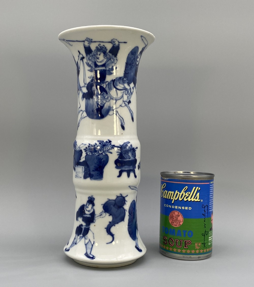 A tall, slender Chinese porcelain beaker vase painted in underglaze cobalt blue featuring equestrian figures and traditional motifs against a smooth white glaze. View II