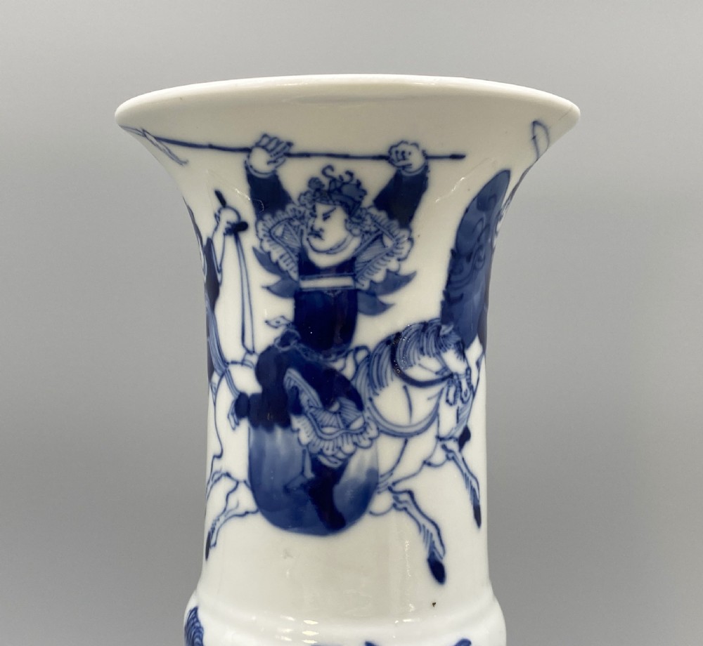 A tall, slender Chinese porcelain beaker vase painted in underglaze cobalt blue featuring equestrian figures and traditional motifs against a smooth white glaze. View III
