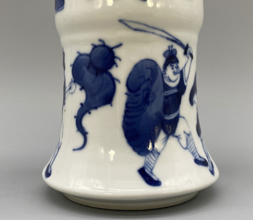 A tall, slender Chinese porcelain beaker vase painted in underglaze cobalt blue featuring equestrian figures and traditional motifs against a smooth white glaze. View IX