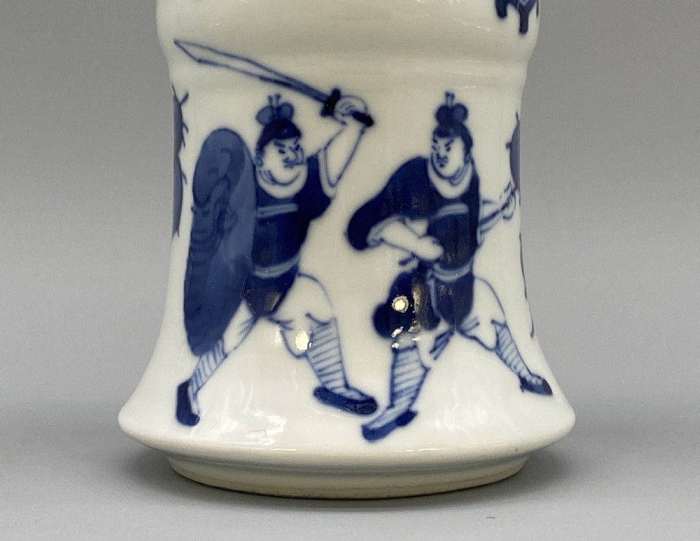 A tall, slender Chinese porcelain beaker vase painted in underglaze cobalt blue featuring equestrian figures and traditional motifs against a smooth white glaze. View X
