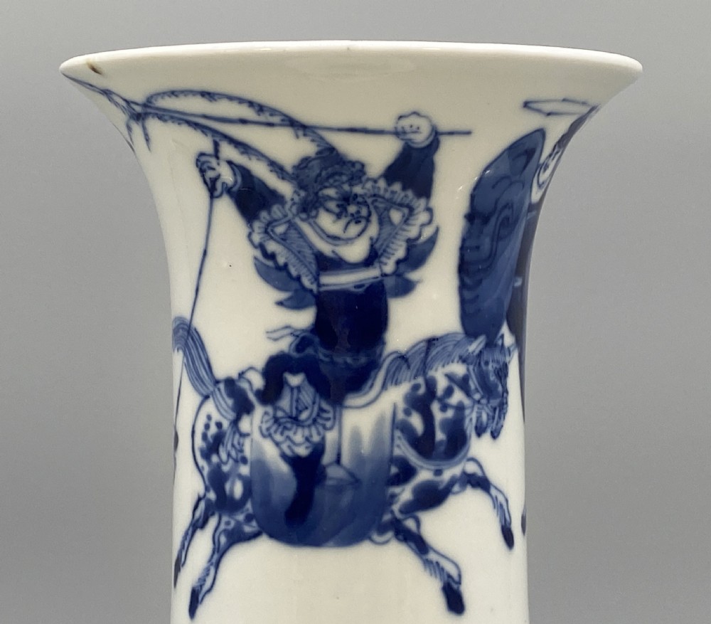 A tall, slender Chinese porcelain beaker vase painted in underglaze cobalt blue featuring equestrian figures and traditional motifs against a smooth white glaze. View XII