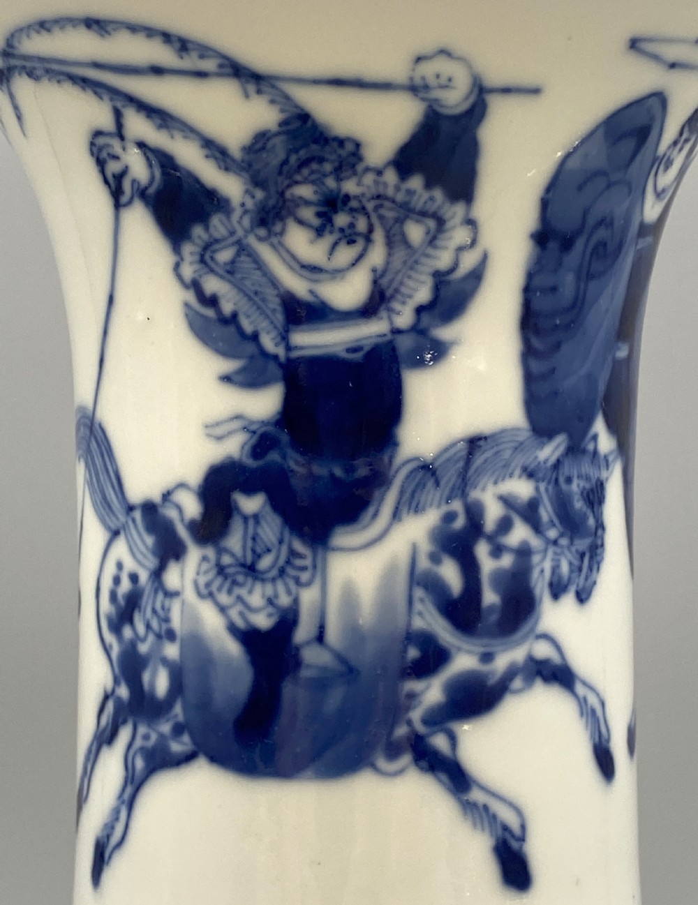 A tall, slender Chinese porcelain beaker vase painted in underglaze cobalt blue featuring equestrian figures and traditional motifs against a smooth white glaze. View XIII