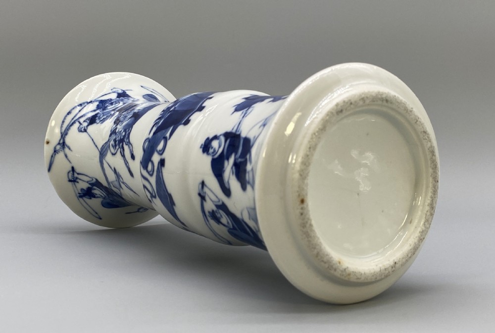 A tall, slender Chinese porcelain beaker vase painted in underglaze cobalt blue featuring equestrian figures and traditional motifs against a smooth white glaze. View XIX