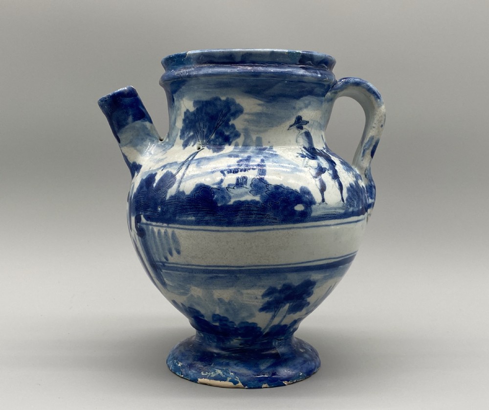 An 18th-century Italian Savona majolica wet drug jar featuring hand-painted cobalt blue landscapes, a single side handle, a raised spout, and a pedestal base. View II